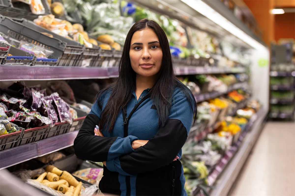 Ung kvinna som jobbar i butik, står med armarna i kors och har ett bestämt uttryck.