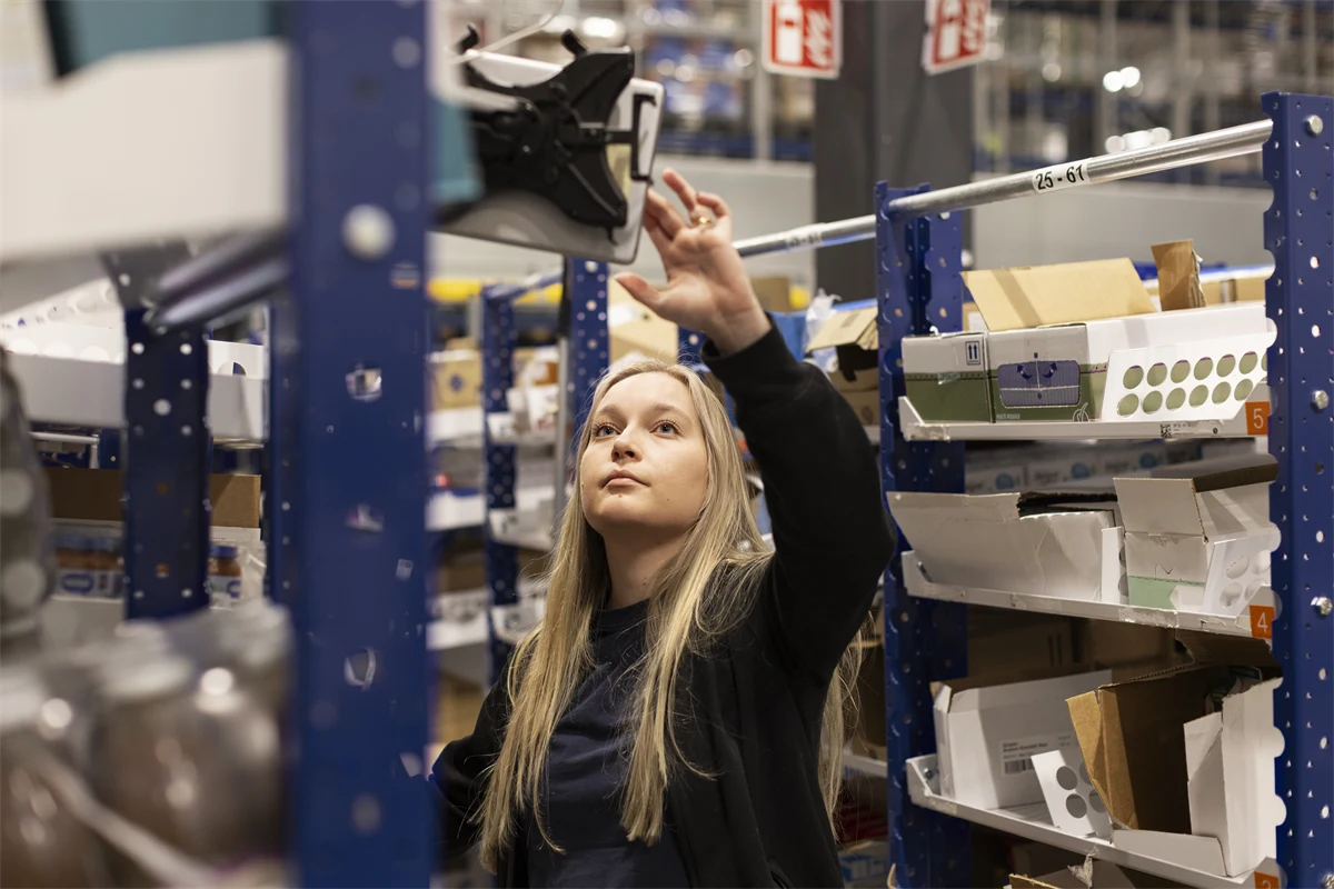Ung kvinna som jobbar på lager, registrerar varor på en skärm.