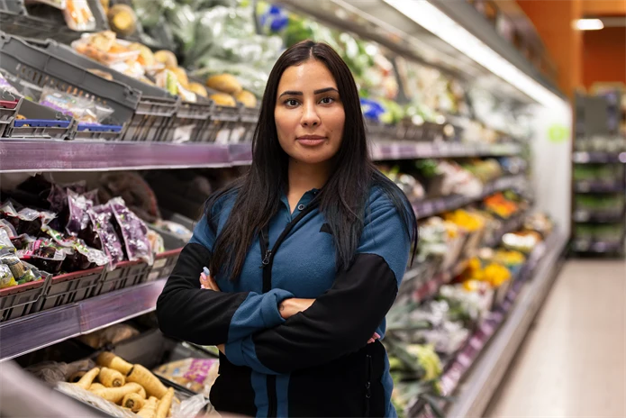 Ung kvinna som jobbar i butik, står med armarna i kors och har ett bestämt uttryck.