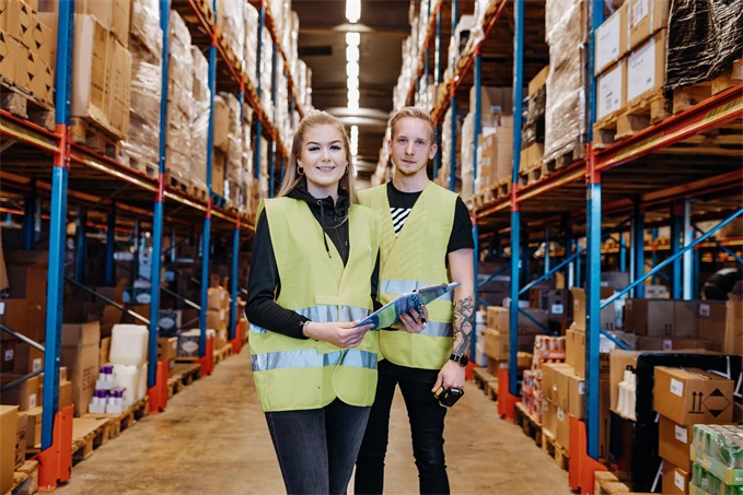 En ung kvinna och ung man som arbetar på lager, iklädda reflexväst.